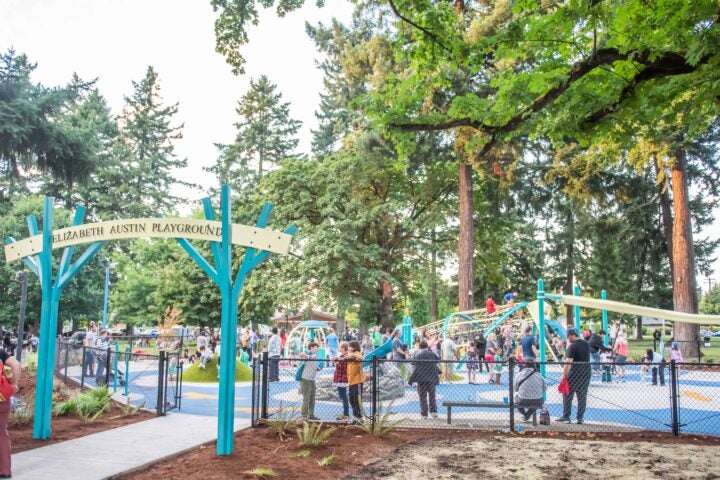 Children playing on a brightly colored, fenced playground with spinners, climbers and a zipline track ride.