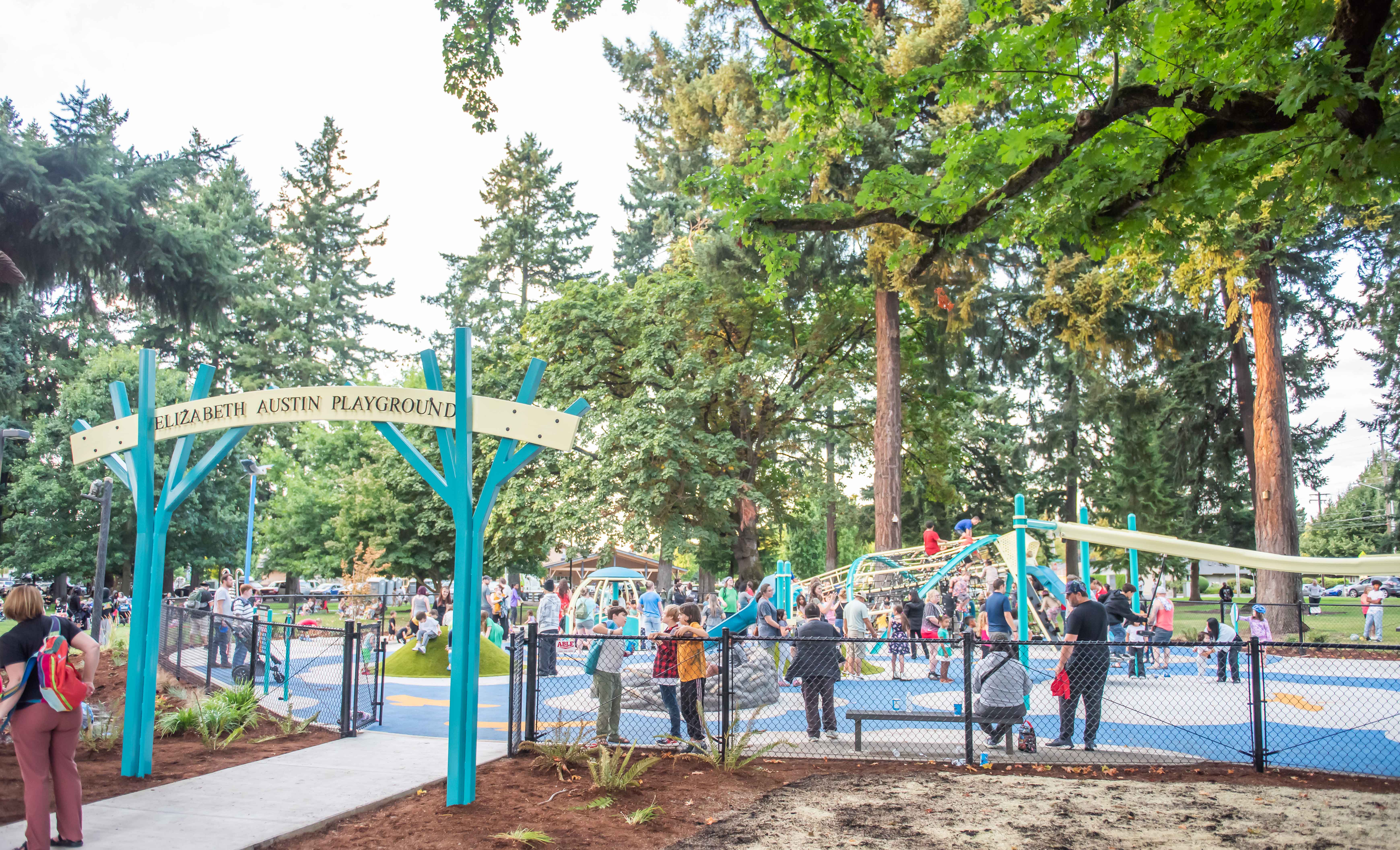Children playing on a brightly colored, fenced playground with spinners, climbers and a zipline track ride.