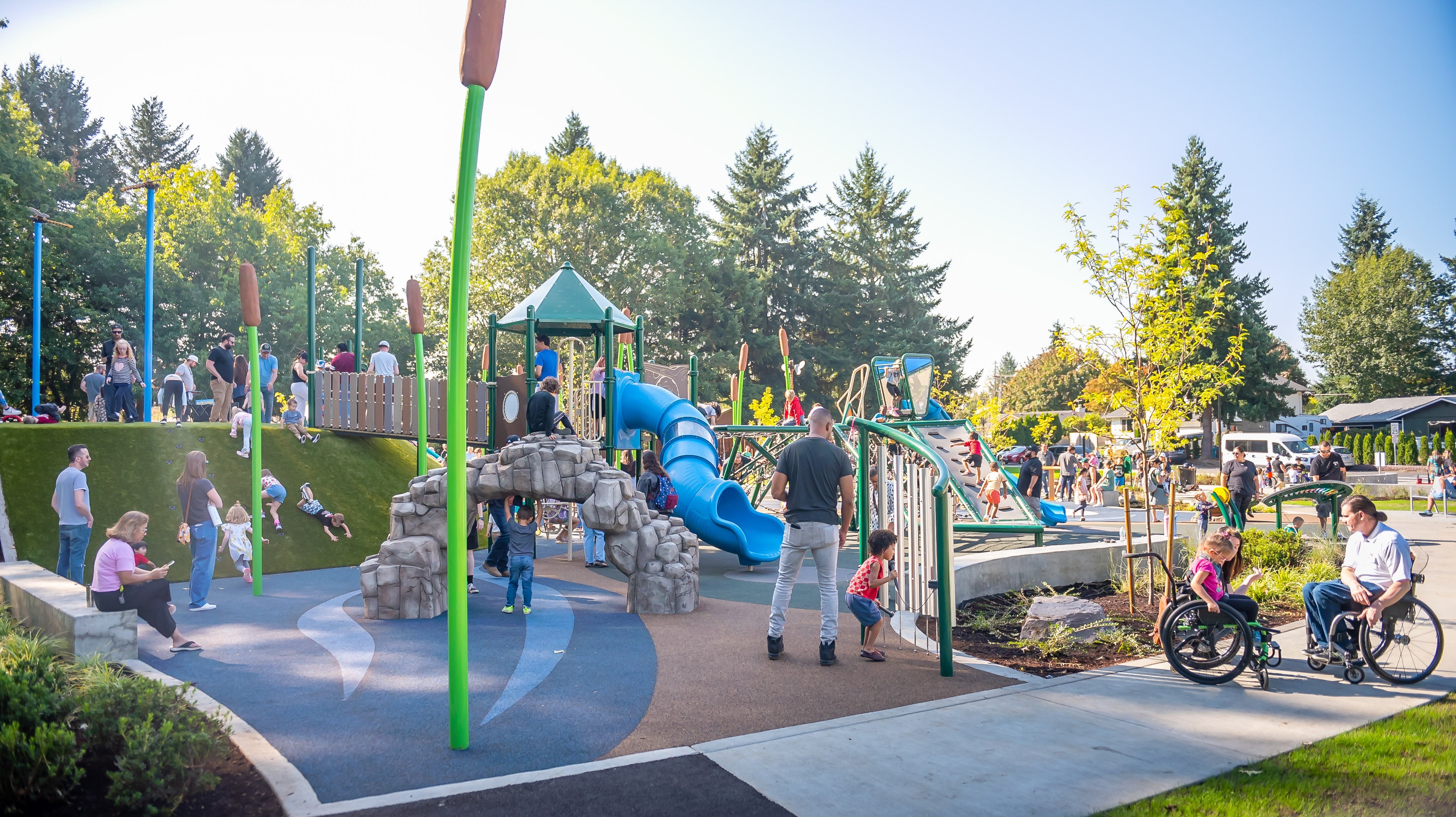 Kids playing on a bright playground with a large hill, slides, musical instruments and wetlands-themed decoration.