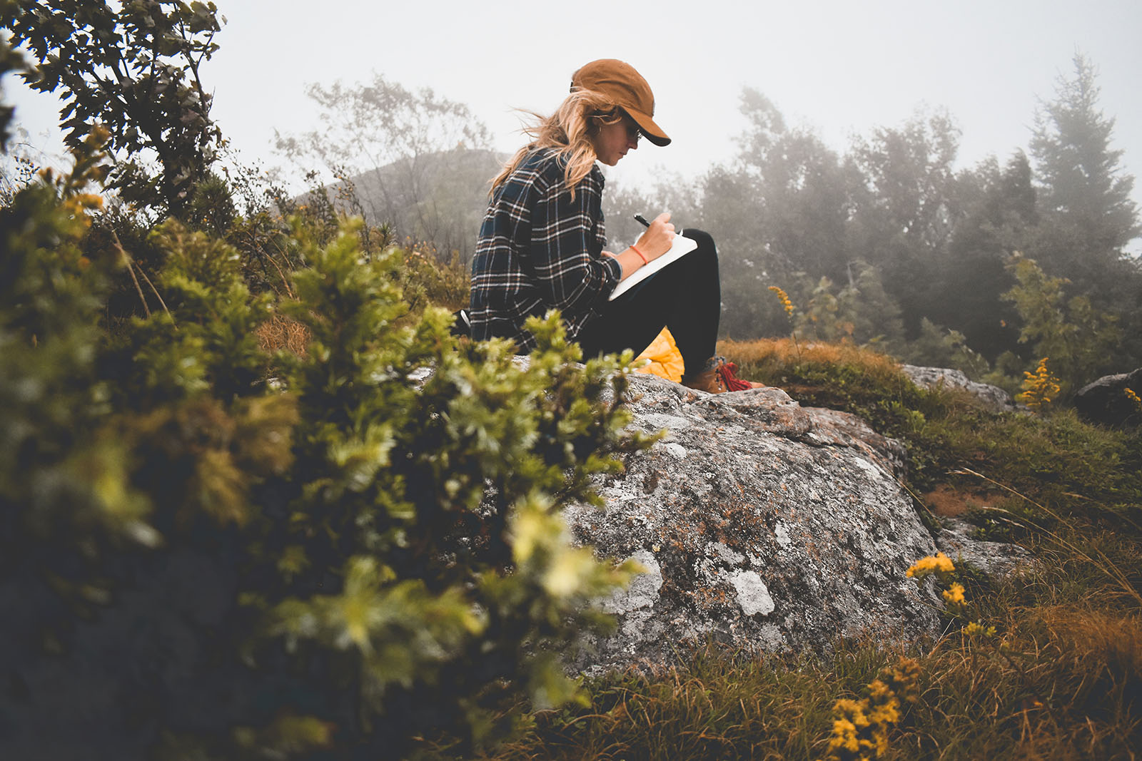 Girl writing in journal on rock in nature