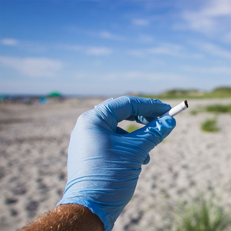 picking up cigarette trash at the beach with a glove