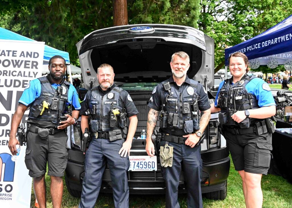 Four Vancouver Police Officers in front of a patrol vehicle at a community event in Esther Short Park