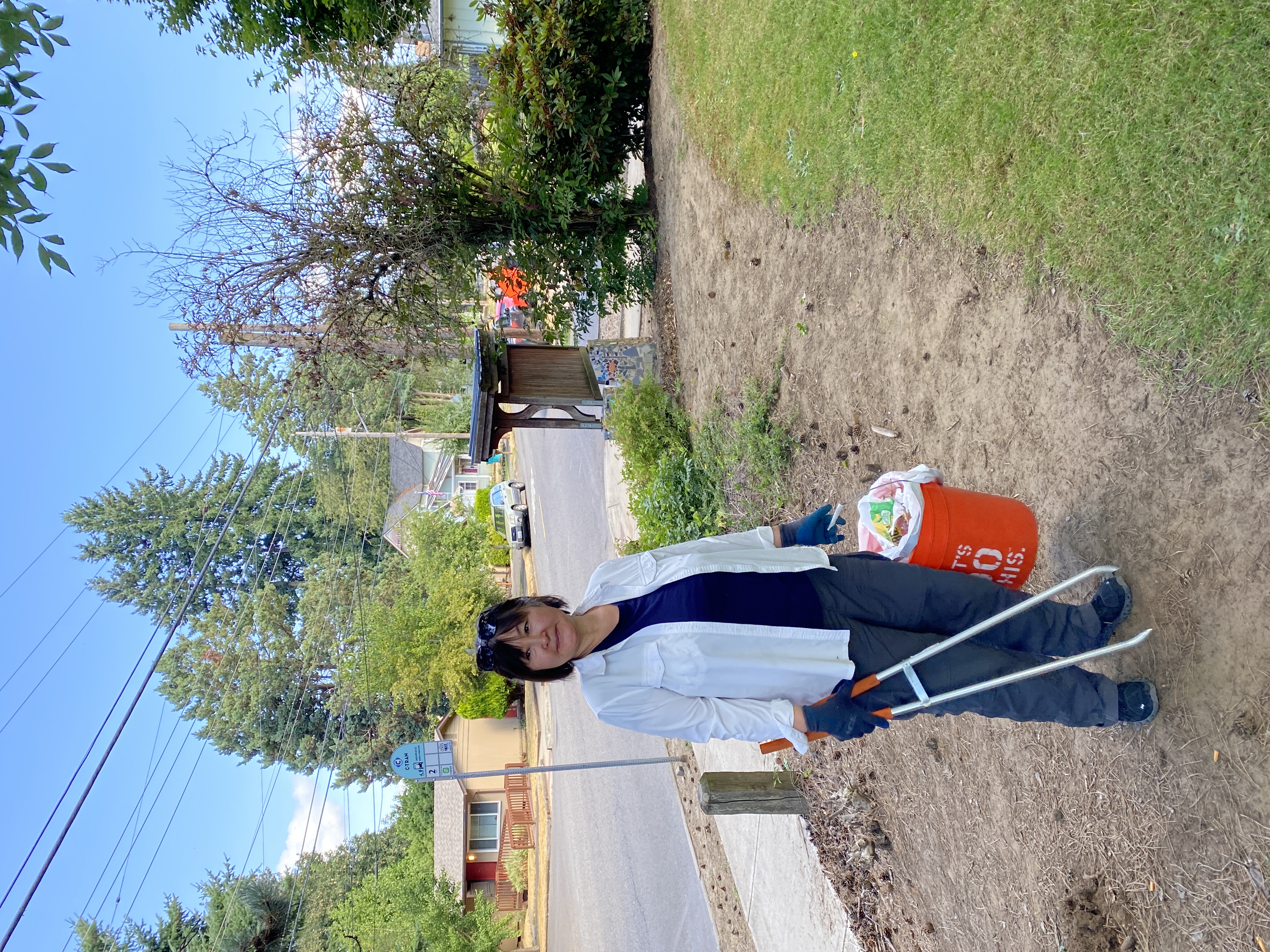 volunteer poses with litter grabber and bucket in park