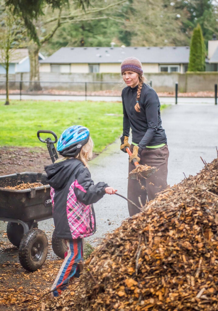 adult volunteer shovels wood chips and child volunteer holds stick