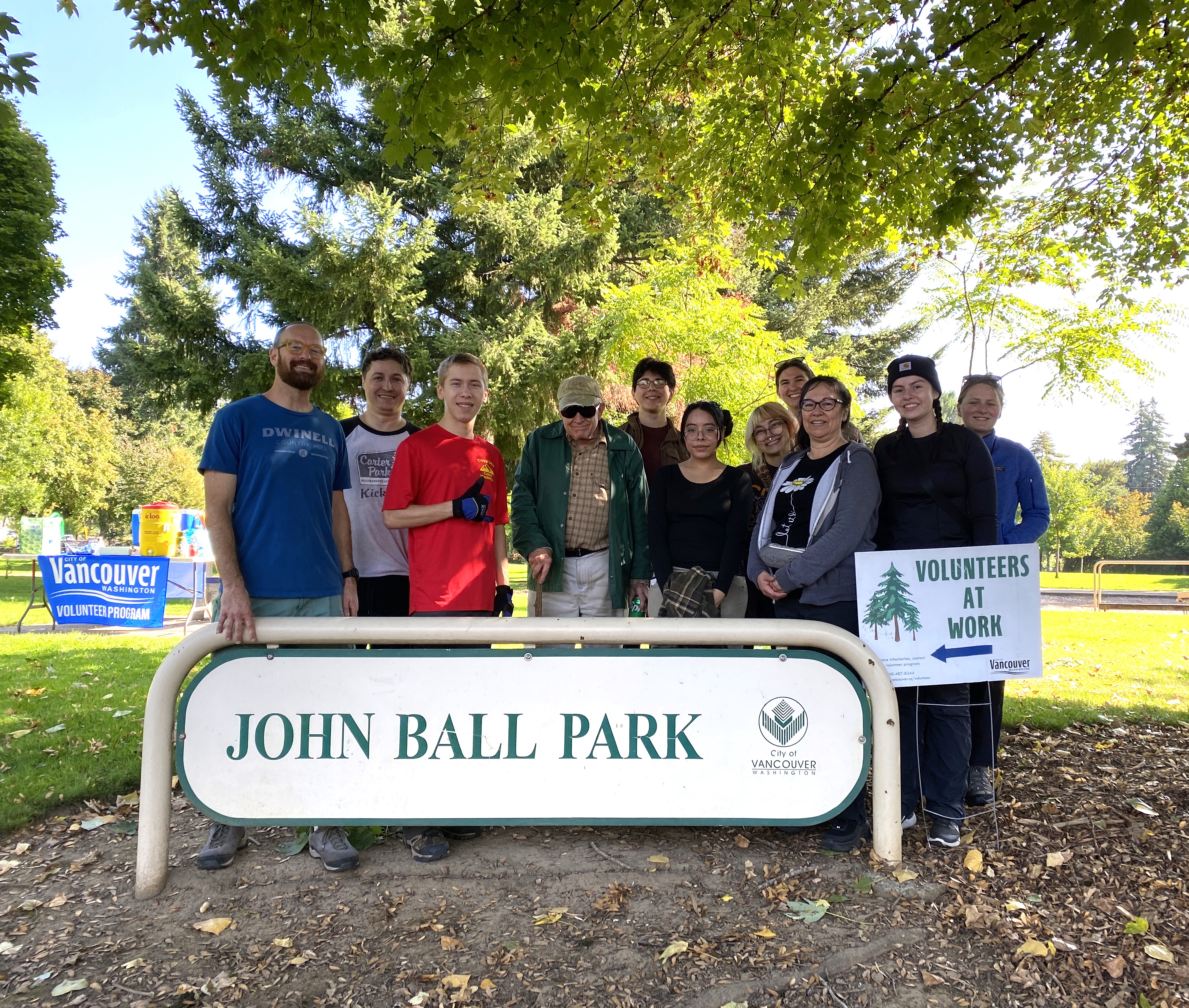 group of volunteers poses around a John Ball Park sign and a Volunteers at Work sign