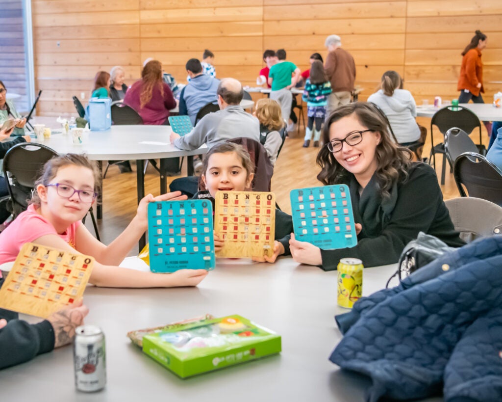 Family smiles while they hold up their Bingo cards at Firstenburg Center Bingo Night
