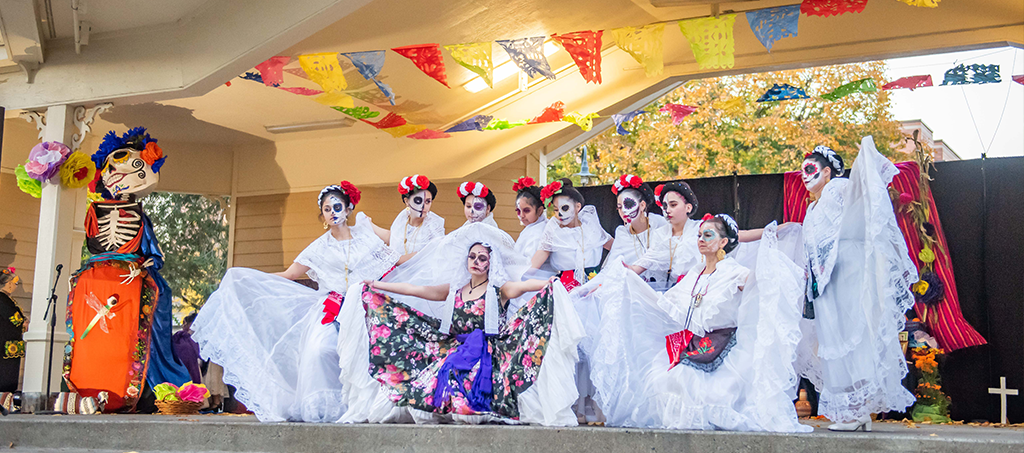 A large group of folklorico dancers perform on an outdoor stage.