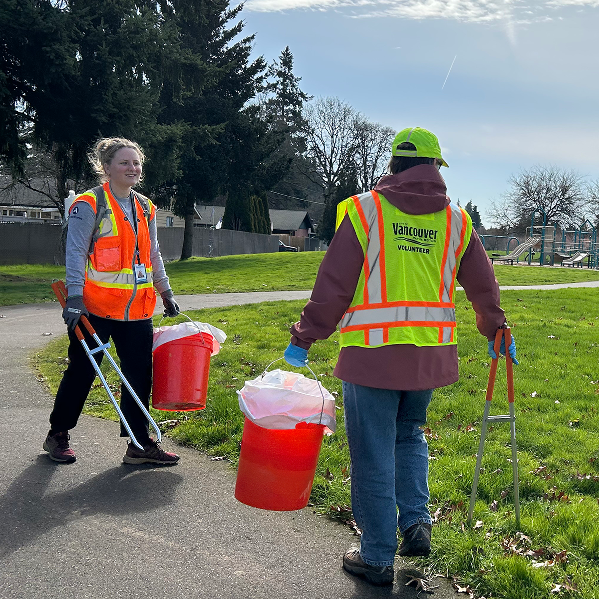 Two volunteers picking up litter at local park with playground in background