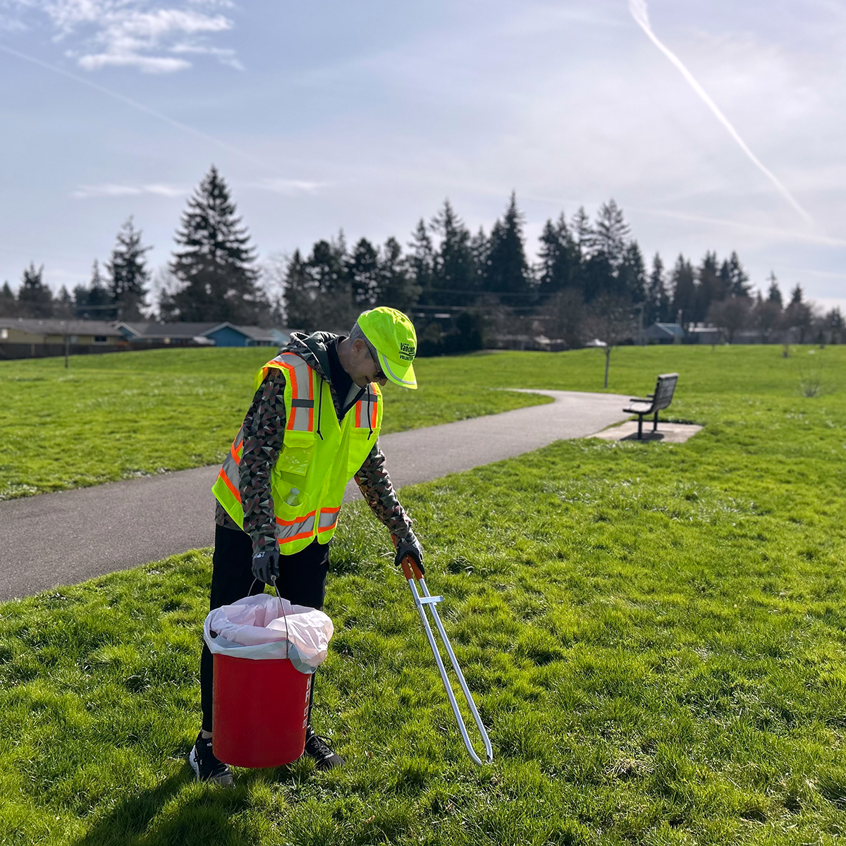 Volunteer picking up litter at local park with bench in background