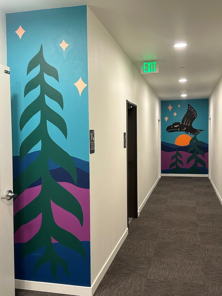 An interior hallway to an apartment building. The walls are painted with vibrant tribal artwork. 