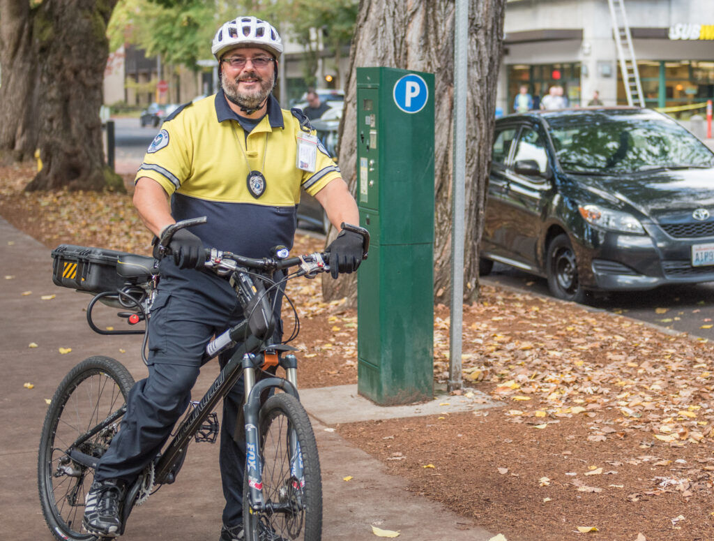 Tim Brown, parking enforcement officer on a bike downtown near a parking meter