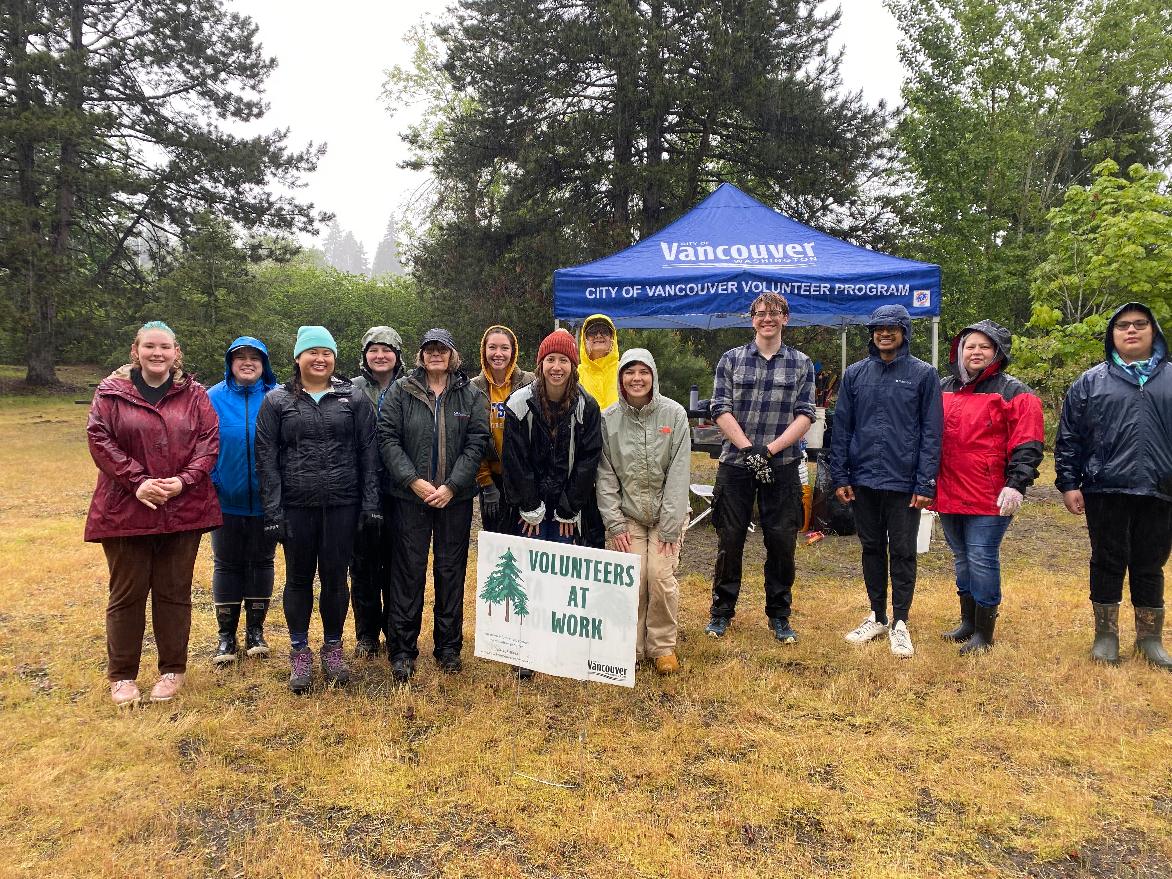 group of volunteers pose with Volunteers at Work sign and a blue canopy in the background