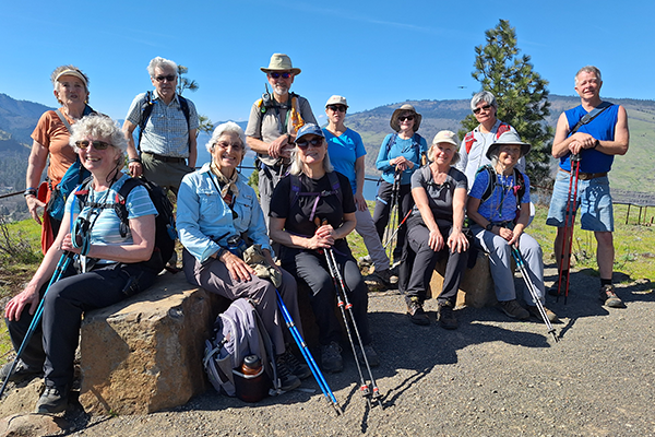 A group of smiling older hikers posing for a photo on an outdoor trail.