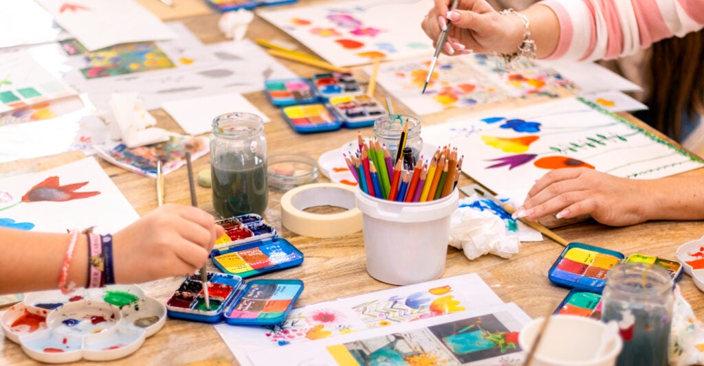 Hands using paint and art supplies on a table.