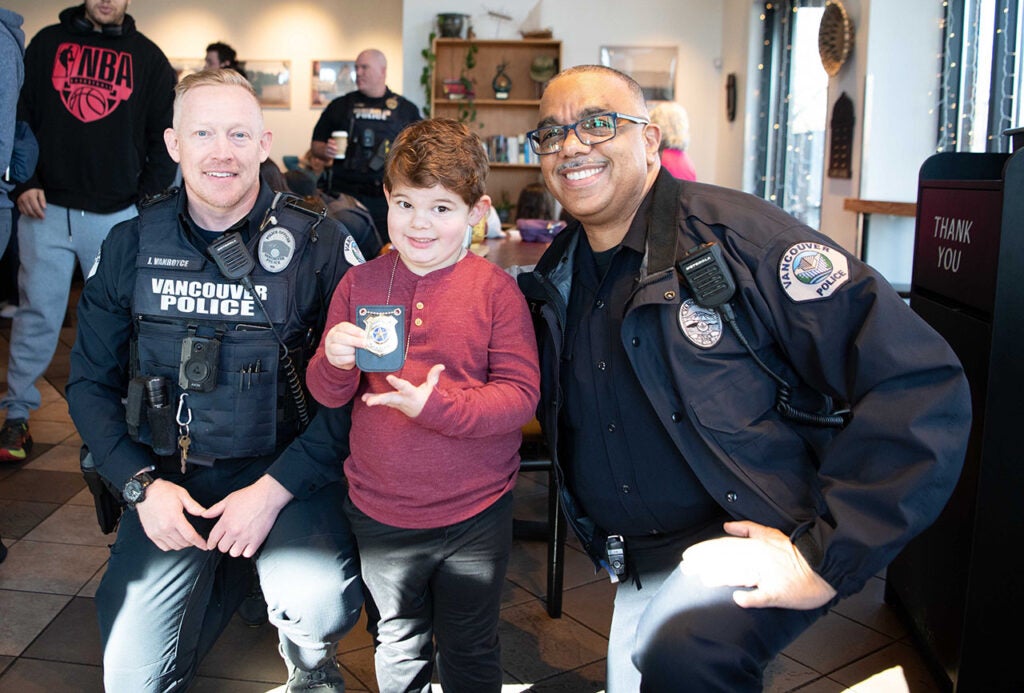 Chief and officer pose with young boy holding official badge