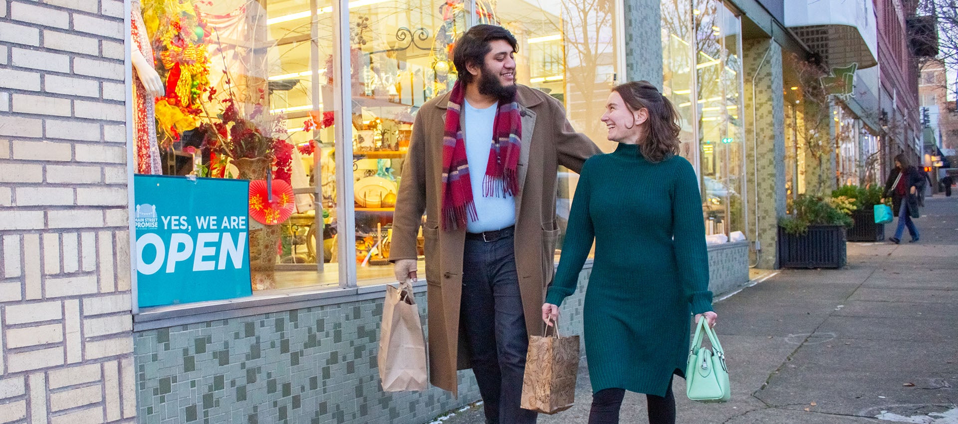 Couple walks down Main Street near business with Open sign in window