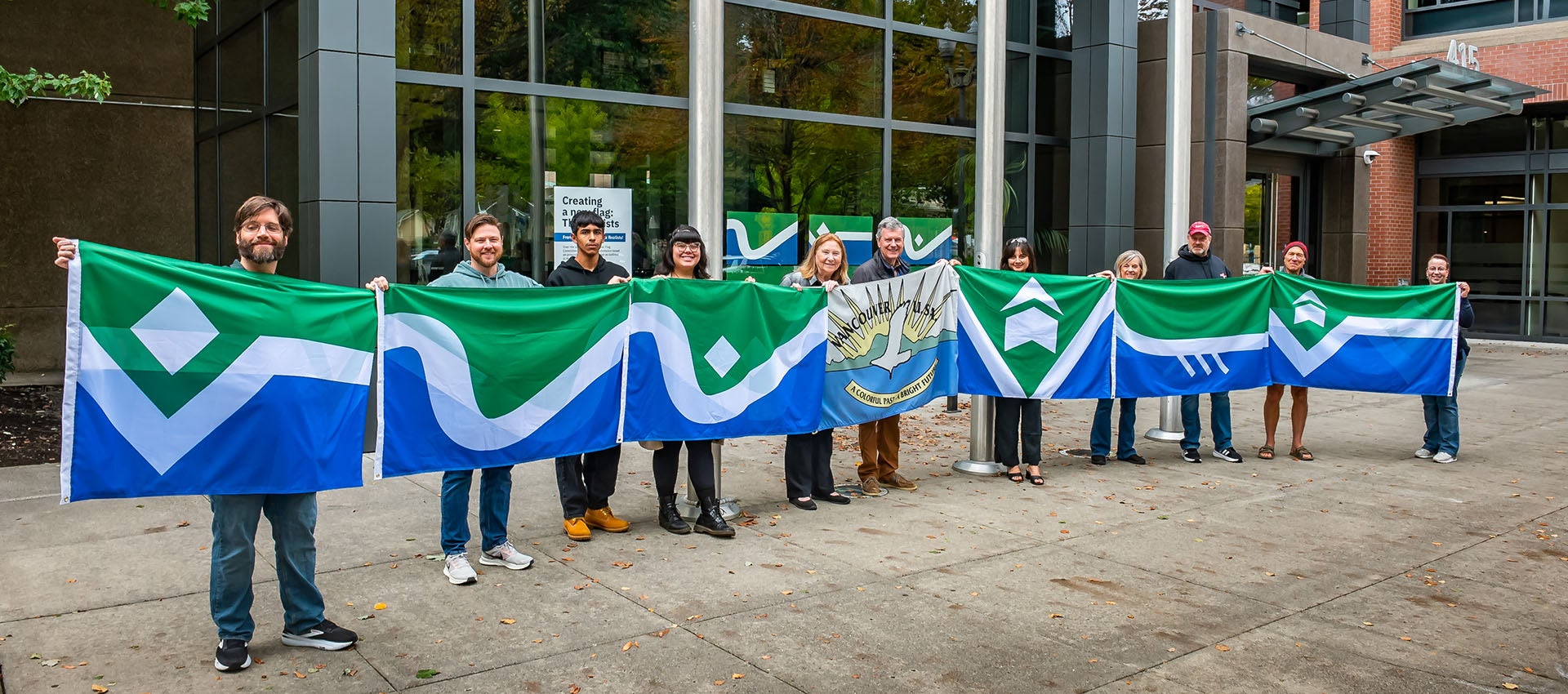 Flag finalists and flag selection committee members pose in front of City Hall with the old flag and the new designs.