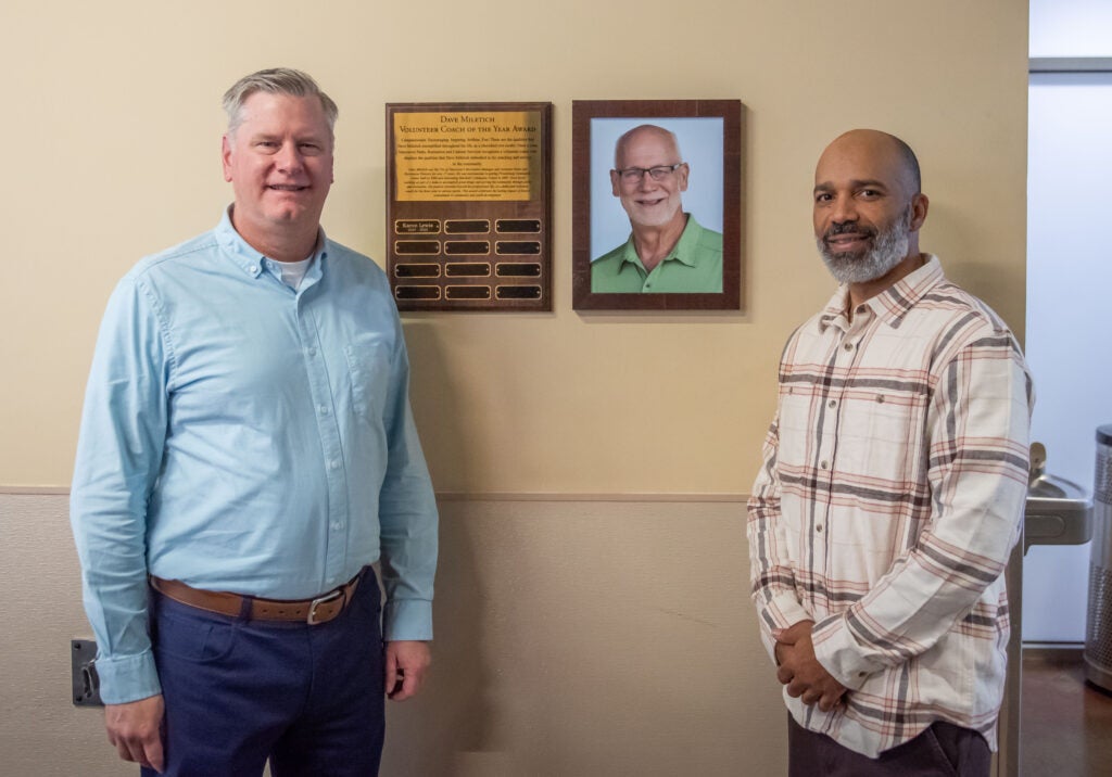 Director David Perlick and Award Winner Karon Lewis in front of the Dave Miletich Coach of the Year award display at Firstenburg