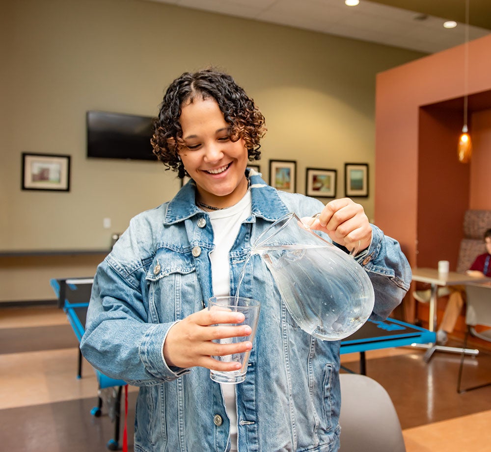 A young person pours water into a glass