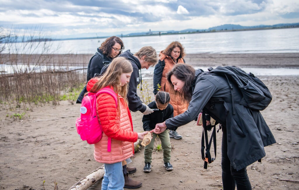 People on the beach next to the river looking at something they found.