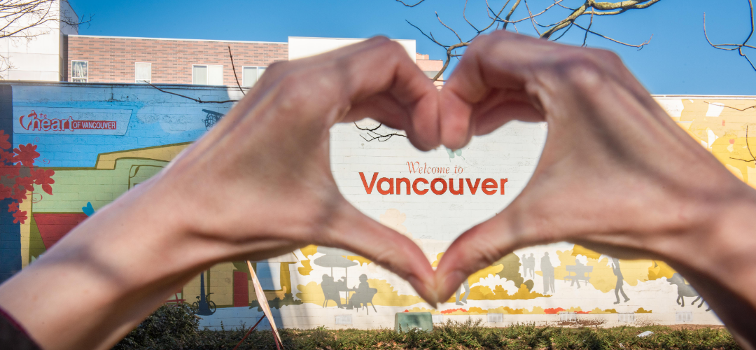 A person holding their hands in a heart shape over a "Welcome to Vancouver" mural.