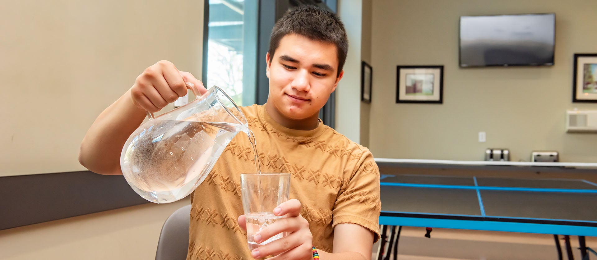 Kid pouring pitcher of water into glass.