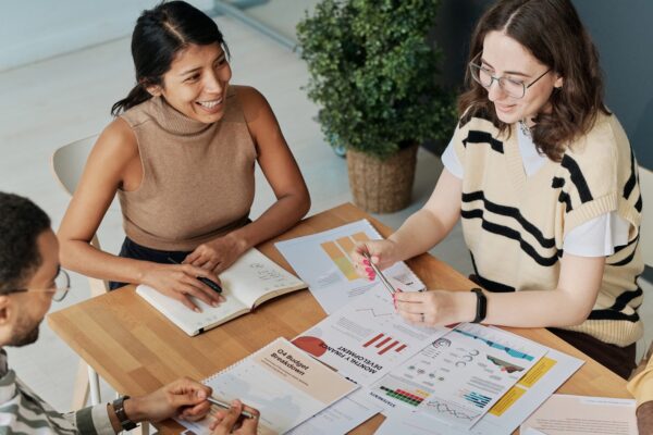 A group of people sit at a table, reviewing multiple documents with various informational charts and diagrams.