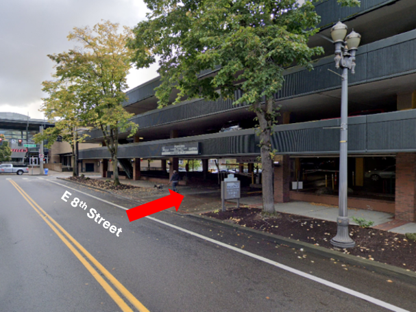 Google maps street view of the entrance of the 703 Broadway parking lot, a red arrow indicating the entry point on East 8th Street.