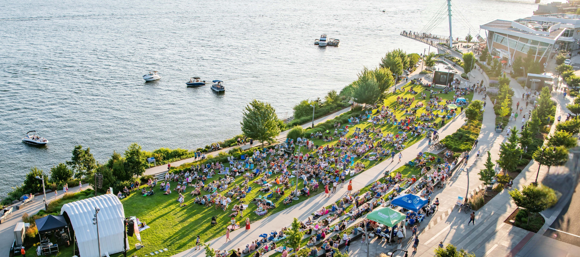 Aerial view of Vancouver Waterfront Park with a stage, crowd covering the lawn, at a summer concert overlooking the Columbia River.
