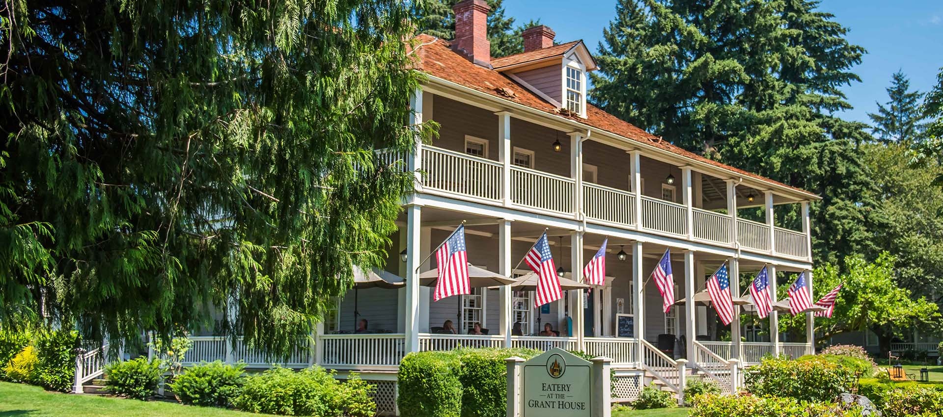 Eatery at the Grant House on sunny day with an American flag on each of the 8 front porch posts.