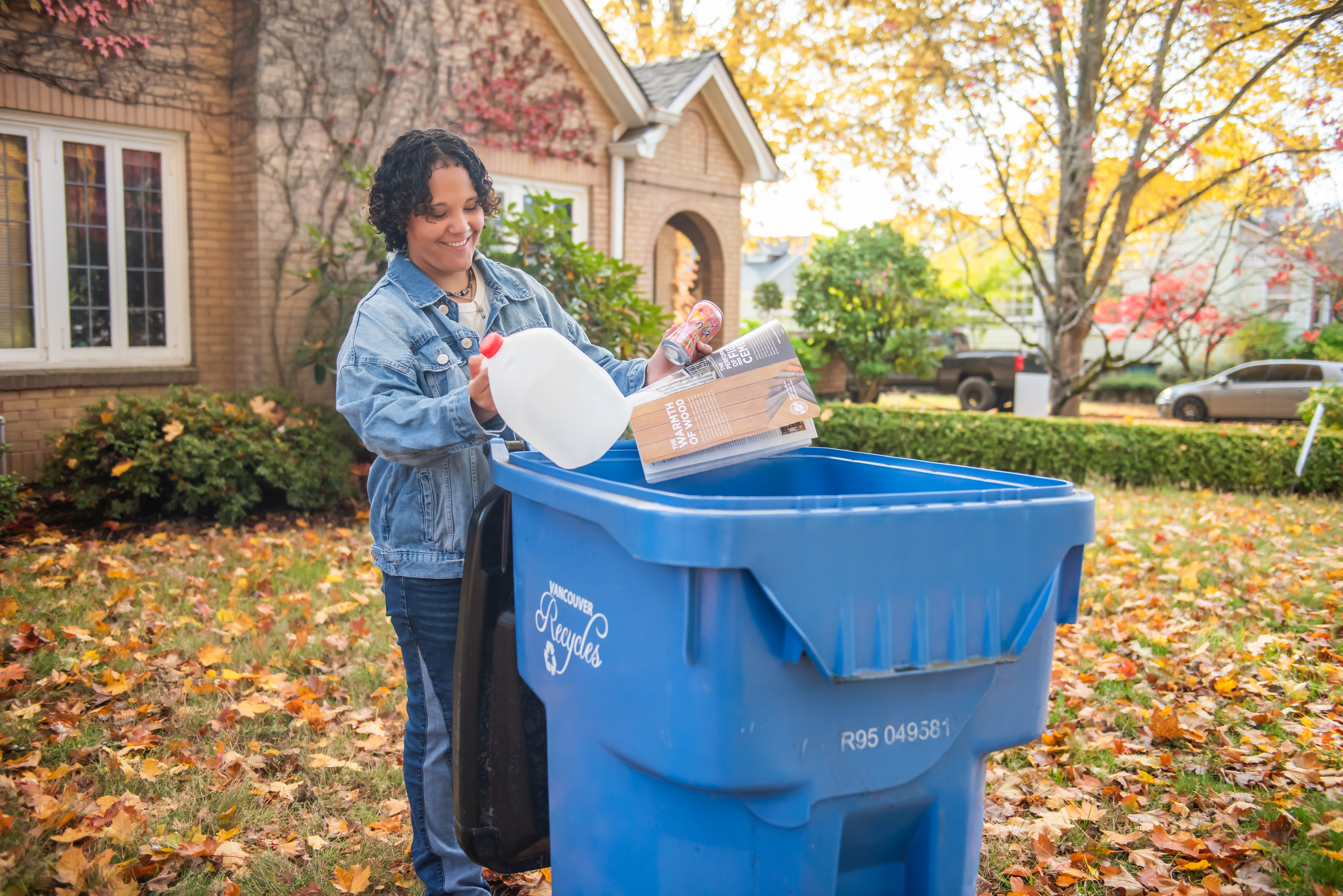 A woman putting items into a blue recycling bin.