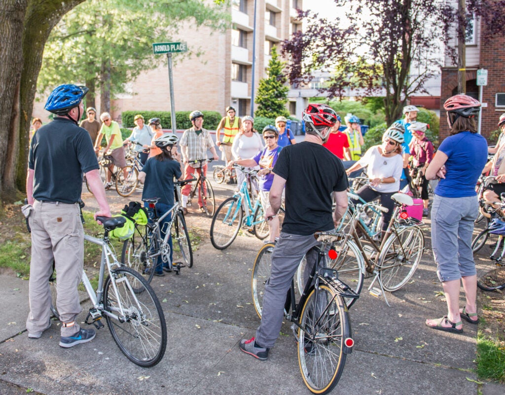 People with bicycles gathered on the corner of a street.