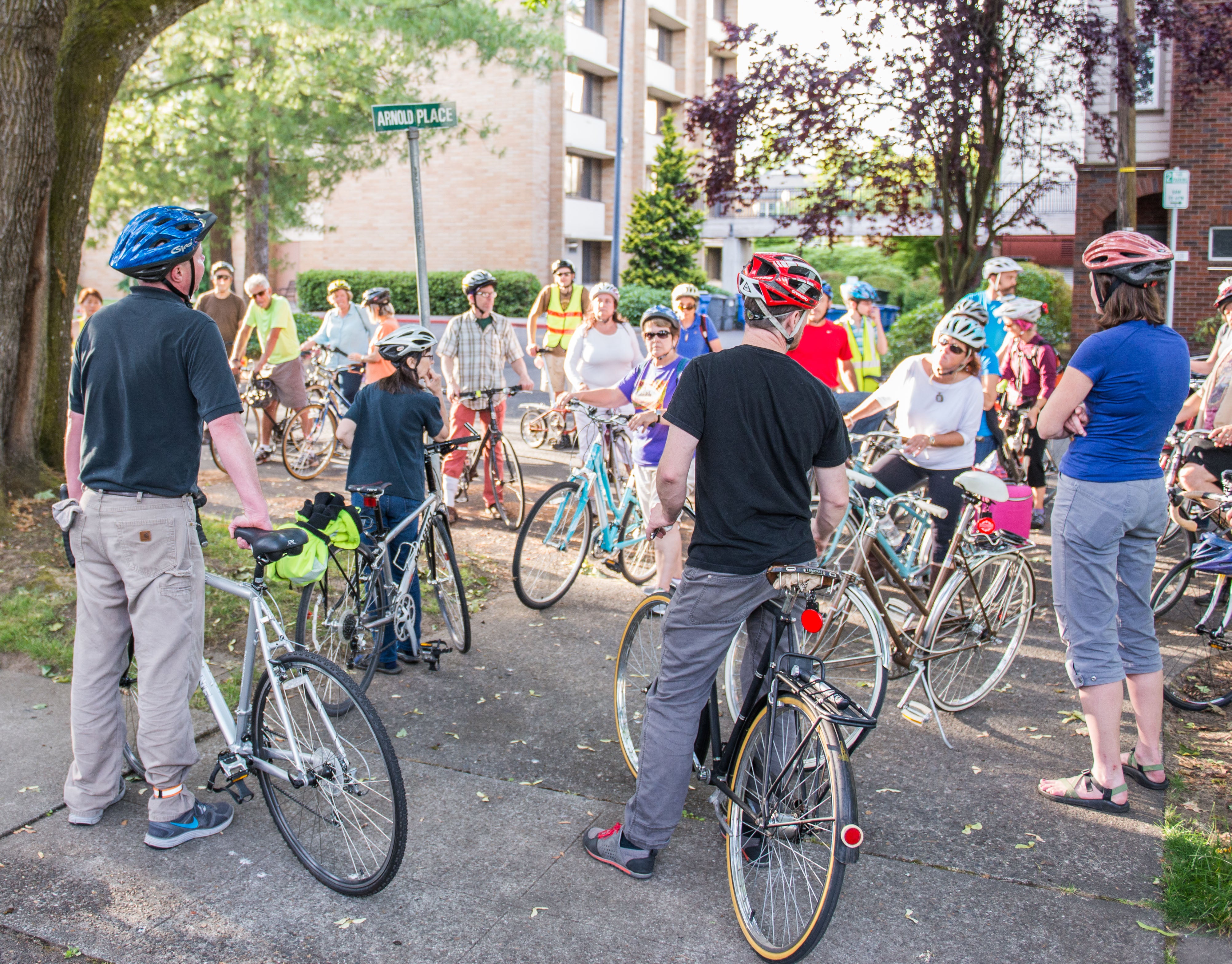 People with bicycles gathered on the corner of a street.