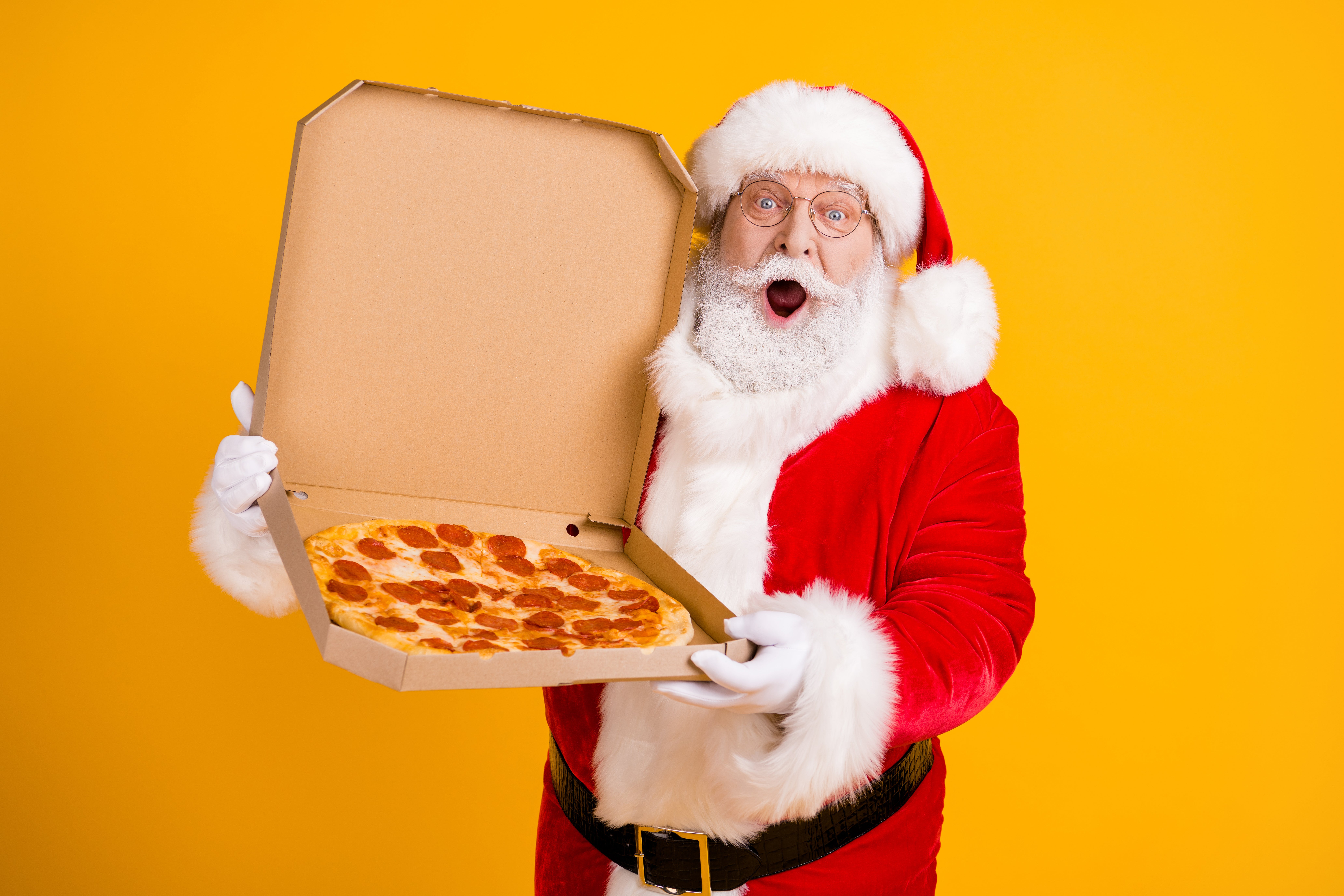 Santa Claus holding up a pizza in a box against a yellow background