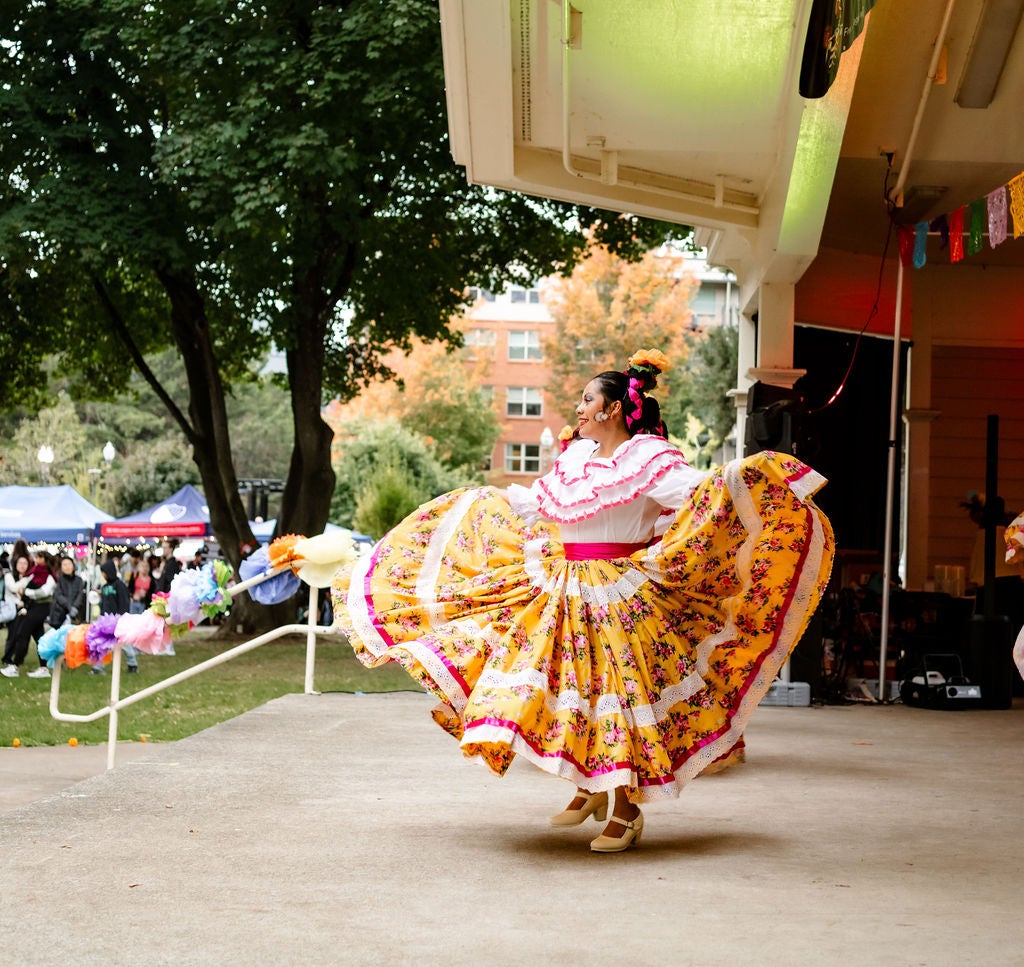 A dancer in a brightly colored skirt performs on an outdoor stage.