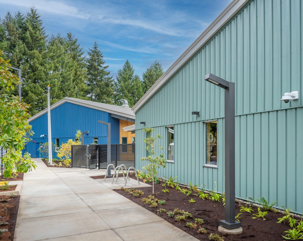 Two buildings at the bridge shelter campus. Outside there's lighting, bike racks and a sidewalk.