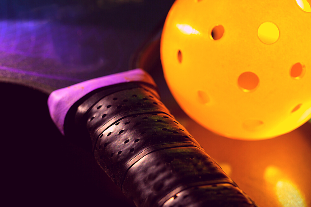 Pickleball paddle and ball lighting up in bright glow in the dark colors